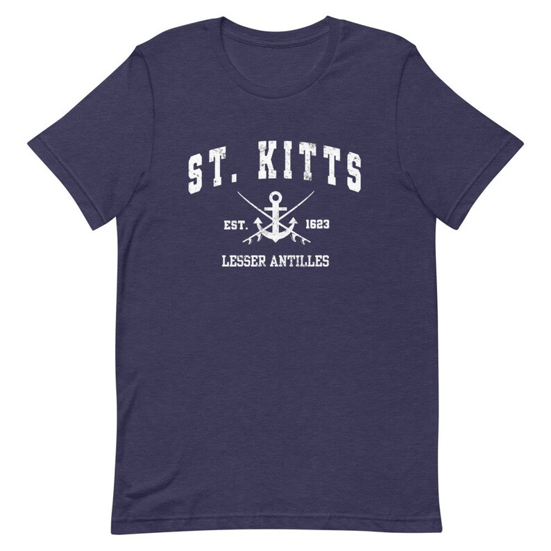 May include: A navy blue t-shirt with a white distressed graphic of the text "ST. KITTS" with an anchor and crossed fishing poles underneath. The text "EST. 1623" and "LESSER ANTILLES" are also included in the graphic.