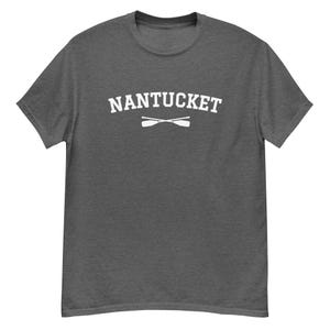 Könnte beinhalten: Ein dunkelgraues T-Shirt mit dem Text "NANTUCKET" in weißen Buchstaben und einem Paar gekreuzter Ruder darunter.