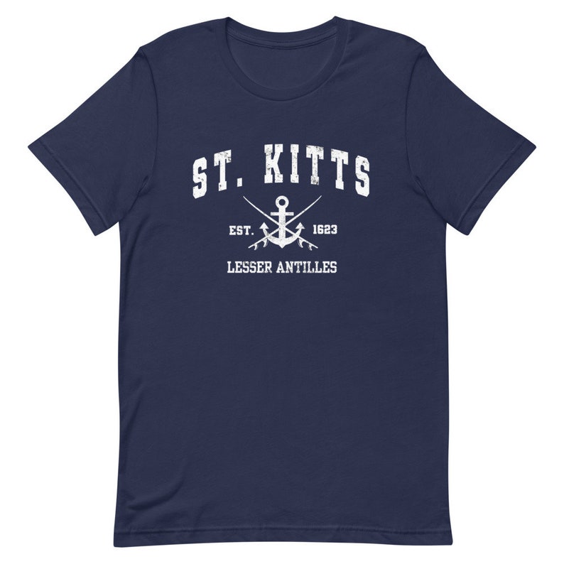 May include: A navy blue t-shirt with a white graphic design. The graphic features the text "ST. KITTS" in a vintage collegiate font, an anchor with crossed oars, and the text "EST. 1623 LESSER ANTILLES".
