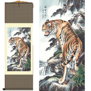 May include: A traditional Chinese scroll painting depicting a tiger in a forest setting. The tiger is depicted in a realistic style with detailed fur markings. The background features a waterfall and trees. The scroll is mounted on a wooden dowel and has a hanging cord.