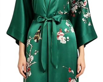 May include: Emerald green satin kimono robe with a floral and bird print. The robe features a tie waist and wide sleeves. The design includes white and red blossoms and a bird perched on a branch.