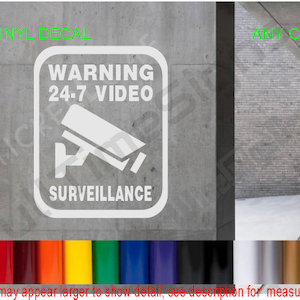 May include: White vinyl decal with a black and white camera icon and the text "WARNING 24-7 VIDEO SURVEILLANCE".