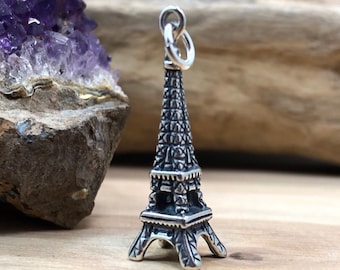 May include: A silver charm in the shape of the Eiffel Tower. The charm is detailed and has a textured surface.