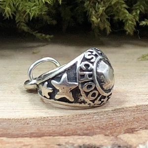 May include: Silver charm in the shape of a class ring with the word "SCHOOL" engraved on the side and two stars.