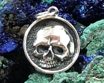 May include: A silver skull pendant charm with a detailed design. The pendant is round and has a textured surface.