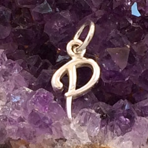 May include: A silver charm in the shape of the letter "P" is displayed on a bed of purple amethyst crystals.