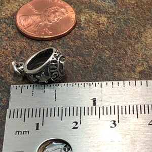 May include: Silver charm in the shape of a class ring with the inscription "HIGH" and a star. The charm is approximately 1 cm in diameter.