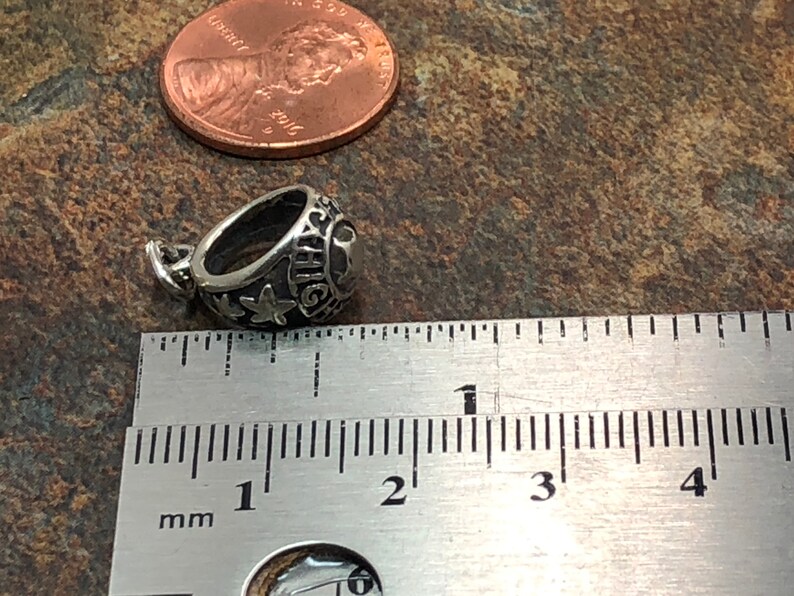 May include: Silver charm in the shape of a class ring with the inscription "HIGH" and a star. The charm is approximately 1 cm in diameter.