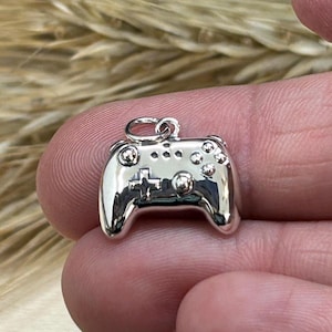 May include: A shiny silver charm in the shape of a video game controller. The charm has detailed buttons and a loop at the top for attaching to a necklace or bracelet. The controller is approximately 1 inch wide.
