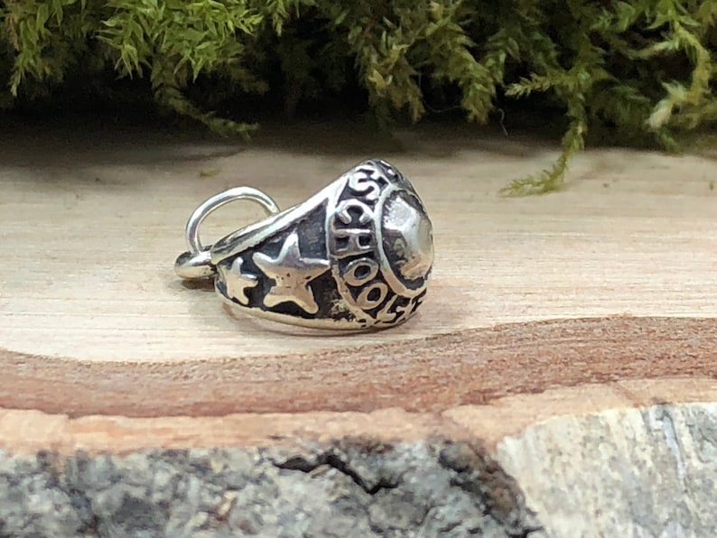 May include: Silver charm in the shape of a class ring with the word "SCHOOL" engraved on the side and two stars.