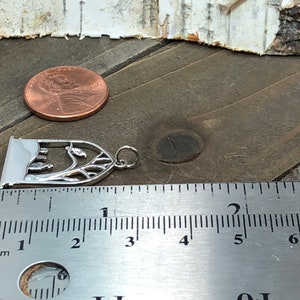 May include: Silver charm featuring a detailed cutout design of a tree with leaves and a small archway. The charm is approximately 2.5 inches long and is shown next to a ruler for size comparison.