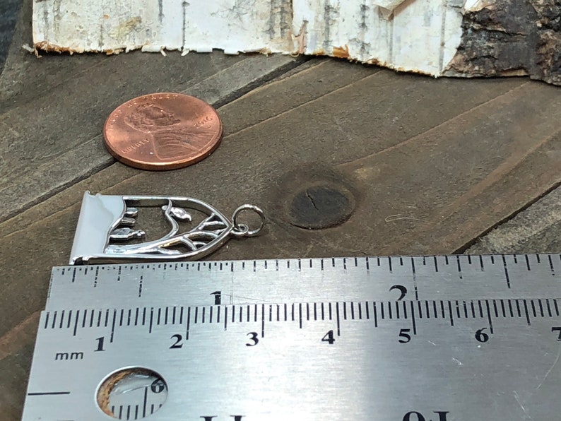 May include: Silver charm featuring a detailed cutout design of a tree with leaves and a small archway. The charm is approximately 2.5 inches long and is shown next to a ruler for size comparison.