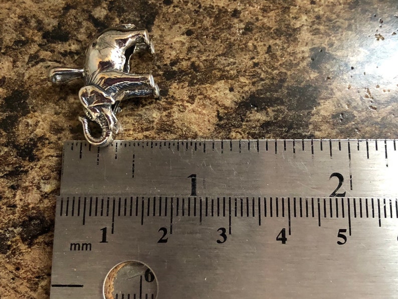 May include: Silver elephant charm pendant measuring approximately 2 cm in length. The charm is detailed with a textured surface and a curled trunk.