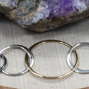 May include: A gold, silver, and black interlocking circle necklace. The circles are of varying sizes and are linked together.
