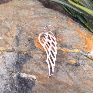 May include: Silver charm in the shape of an angel wing. The wing is detailed with a delicate, intricate design.