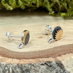 May include: A pair of silver earrings with a black and gold sun and moon design. The earrings have a small loop at the bottom.