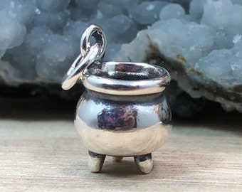 May include: A silver charm in the shape of a cauldron with a loop for attaching to a bracelet or necklace.