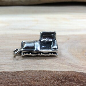 May include: A small, detailed silver charm in the shape of a vintage pickup truck. The charm has a loop for attaching to a bracelet or necklace. The truck features a cab, bed, and wheels, with visible details.