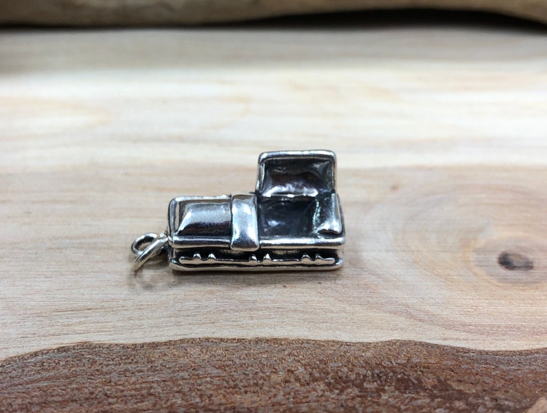 May include: A small, detailed silver charm in the shape of a vintage pickup truck. The charm has a loop for attaching to a bracelet or necklace. The truck features a cab, bed, and wheels, with visible details.