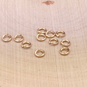 May include: A group of 12 gold jump rings, a type of jewelry finding, on a wooden surface.