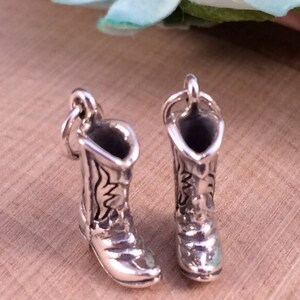 May include: Two silver charm pendants in the shape of cowboy boots. The boots have a detailed design and are a popular charm for jewelry making.