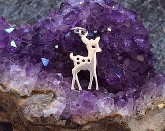 May include: A silver charm in the shape of a deer with spots, resting on a bed of purple amethyst crystals.