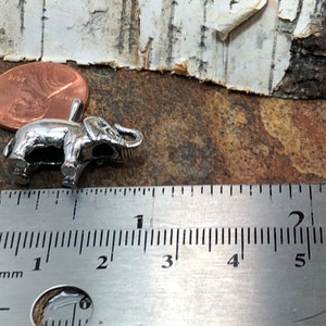 May include: A silver elephant charm measuring approximately 1 inch in length. The charm is shown next to a ruler for size reference.
