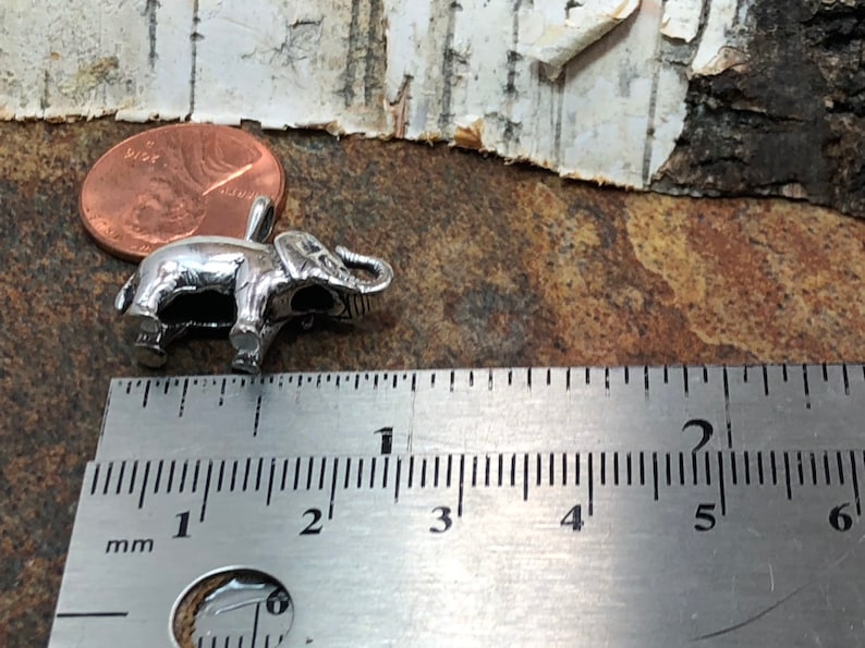 May include: A silver elephant charm measuring approximately 1 inch in length. The charm is shown next to a ruler for size reference.