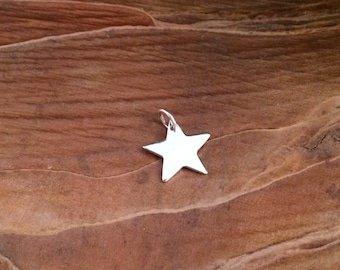 May include: A silver star charm pendant, with a smooth, flat surface. The charm is shown on a brown wooden background.