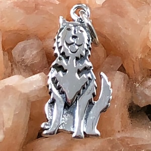 May include: A silver charm in the shape of a wolf, sitting with its head tilted up and its mouth slightly open. The charm is detailed with fur and has a loop at the top for attaching to a necklace or bracelet.