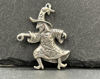 May include: A silver-toned witch pendant with a pointed hat and flowing robe. The witch's robe is adorned with stars and crescent moons. The pendant is detailed with a loop for hanging.