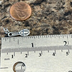 K&ouml;nnte beinhalten: Ein silberner Anh&auml;nger in Form eines kleinen L&ouml;ffels, der etwa 2,5 cm lang ist. Der Anh&auml;nger wird neben einem Lineal zur Gr&ouml;&szlig;envergleich gezeigt.