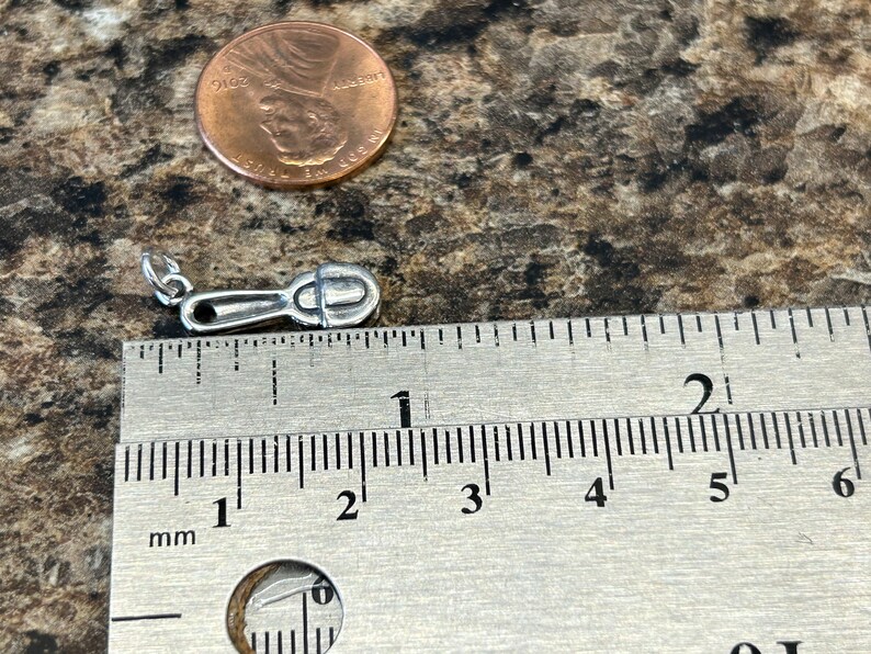 K&ouml;nnte beinhalten: Ein silberner Anh&auml;nger in Form eines kleinen L&ouml;ffels, der etwa 2,5 cm lang ist. Der Anh&auml;nger wird neben einem Lineal zur Gr&ouml;&szlig;envergleich gezeigt.