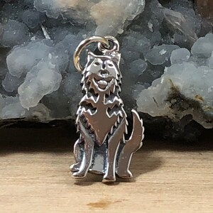 May include: A silver charm in the shape of a wolf sitting with its head tilted up. The charm is detailed with fur and has a realistic look.
