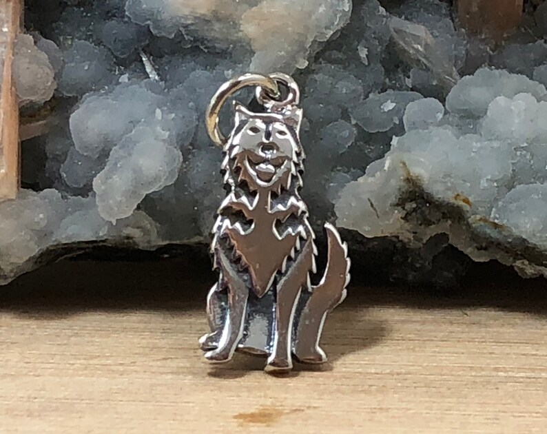 May include: A silver charm in the shape of a wolf sitting with its head tilted up. The charm is detailed with fur and has a realistic look.