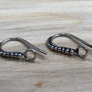 May include: A pair of silver earring hooks with a beaded design. The hooks are made of metal and have a small loop at the end.