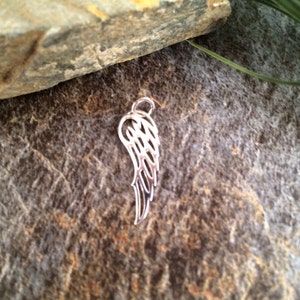 May include: A silver charm in the shape of an angel wing. The wing is detailed with intricate lines and curves.