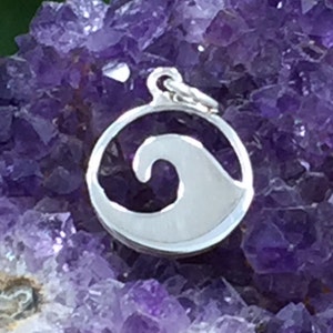 May include: Silver charm pendant featuring a cut-out wave design. The charm is round and has a smooth, polished finish.