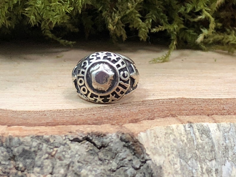 May include: A silver ring with the words "School High" engraved around the band. The ring has a star design and a raised center.