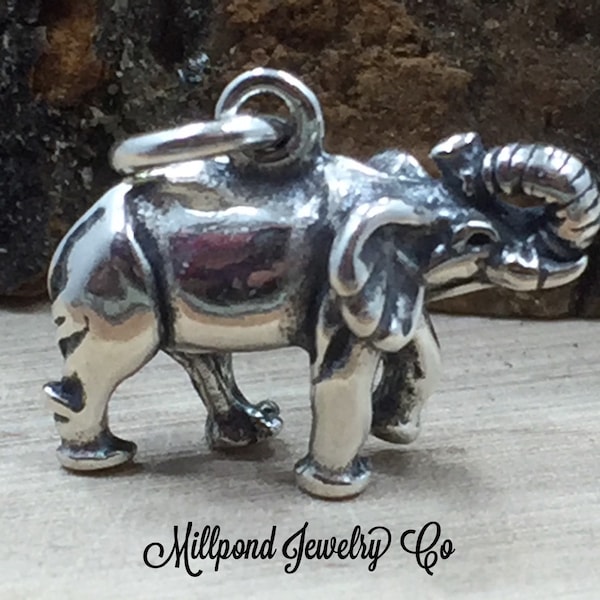 May include: A silver charm in the shape of an elephant with its trunk raised. The charm is detailed with textured features and is suitable for jewelry making.
