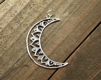 May include: Silver crescent moon pendant with a detailed, ornate design. The moon is surrounded by a border of small, raised dots and intricate floral patterns.