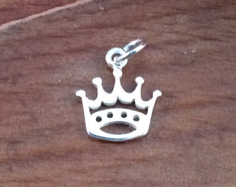 May include: Silver crown charm with a simple design. The charm is a cutout of a crown with five points and a loop at the top for attaching to a necklace or bracelet.