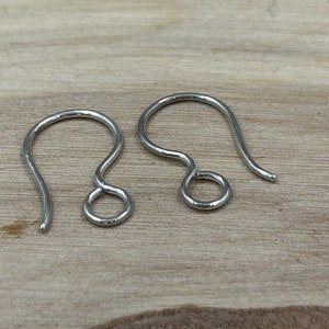 May include: Two silver earring hooks, also known as French hooks, are shown on a wooden surface. The hooks are made of metal and have a smooth finish.