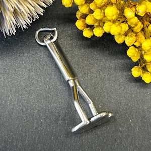 May include: A silver-toned metal charm in the shape of a person with legs spread apart, as if standing on a surface. The charm has a loop at the top for attaching to a necklace or bracelet.