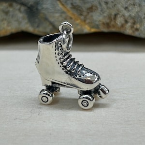 May include: A detailed silver roller skate charm with intricate detailing. The charm features a classic roller skate design, complete with laces, wheels, and a loop for attaching to a bracelet or necklace. The charm is made of a shiny, reflective metal.