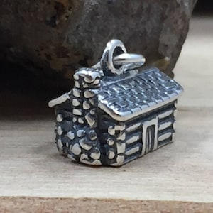 May include: A silver charm in the shape of a small log cabin with a stone chimney. The charm has a detailed design and is perfect for adding a rustic touch to jewelry.