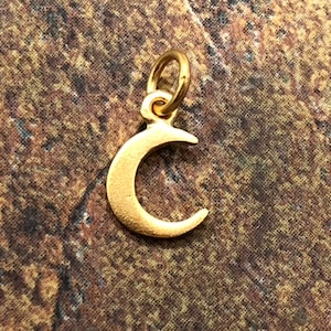 May include: A gold crescent moon charm pendant. The charm is made of metal and has a smooth, polished finish.
