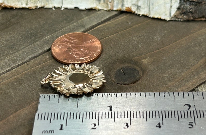 May include: A silver-colored pendant with a floral design, next to a penny and a ruler. The pendant is approximately 0.75 inches in diameter. The ruler shows measurements in millimeters.