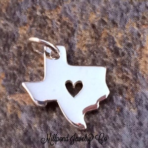 May include: Silver charm in the shape of the state of Texas with a heart cut out in the center.  Millpond Jewelry Co.