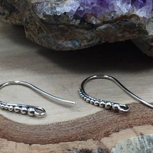 May include: A pair of silver earring hooks with a beaded design. The hooks are made of metal and have a smooth finish.
